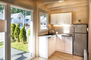 Une cuisine moderne avec des meubles blancs, un réfrigérateur en acier inoxydable et une vue sur un quartier résidentiel avec des maisons et des arbres.