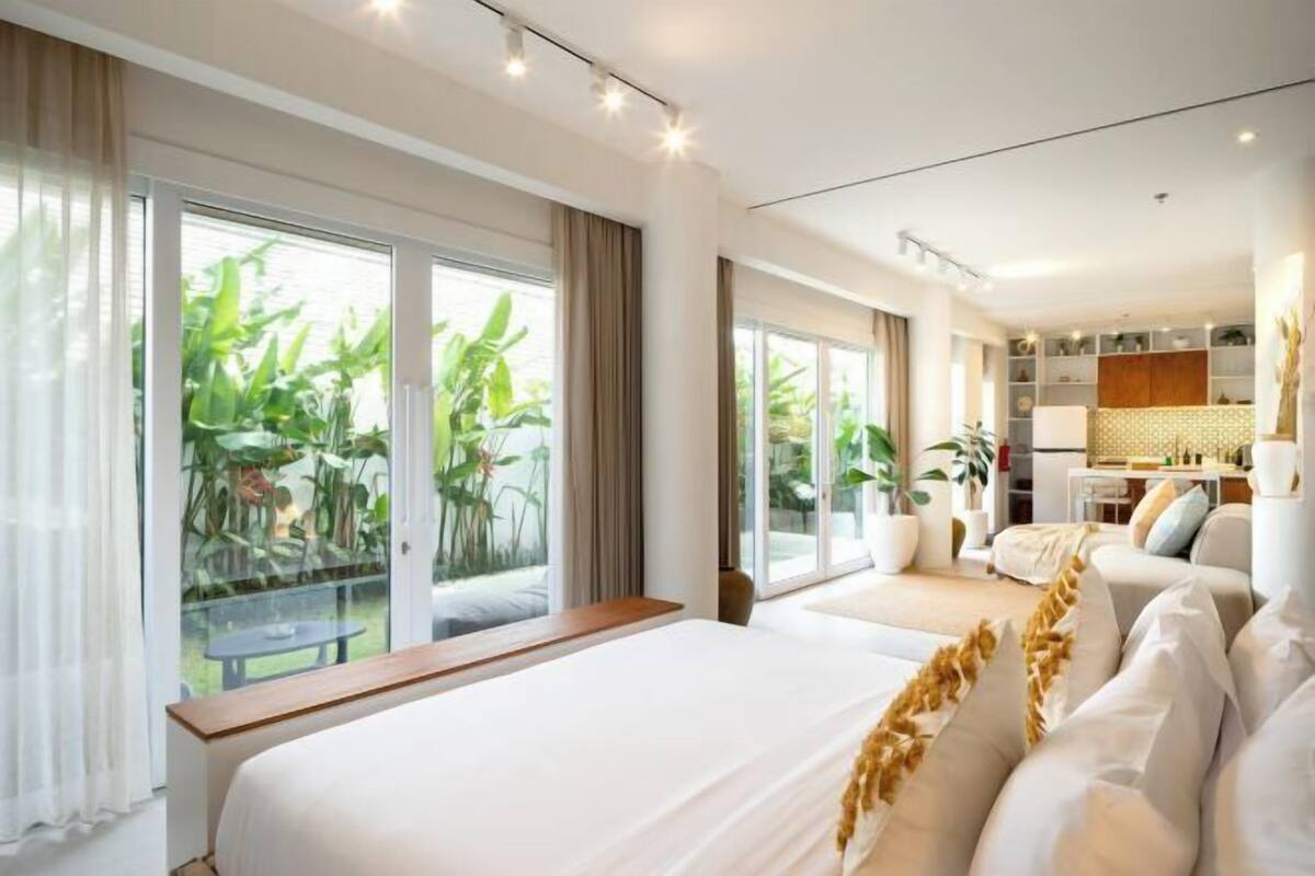 Habitación de hotel con una cama grande, un sofá, zona de comedor y vistas a zonas verdes por las ventanas.