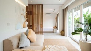 Ein modernes Schlafzimmer mit einem großen Bett, einer Couch und Blick auf Grün hinter großen Fenstern.