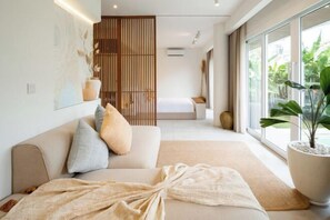 Une chambre moderne avec un grand lit, un canapé et une vue sur la verdure grâce à de grandes fenêtres.
