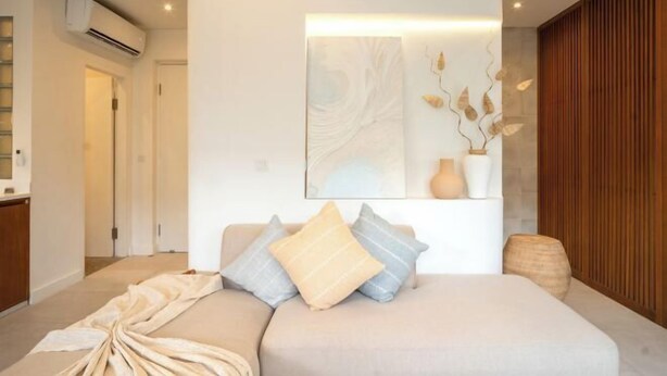 Ein modernes Schlafzimmer mit einer neutralen Farbgestaltung, einem großen Bett mit vielen Kissen, einem Nachttisch mit einer Vase und einem Wandbild.