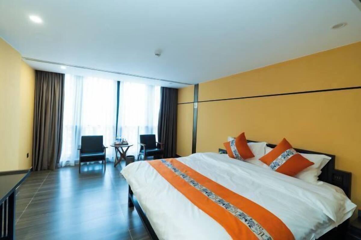 A hotel room with a bed, two chairs, a small table, and a window with curtains.