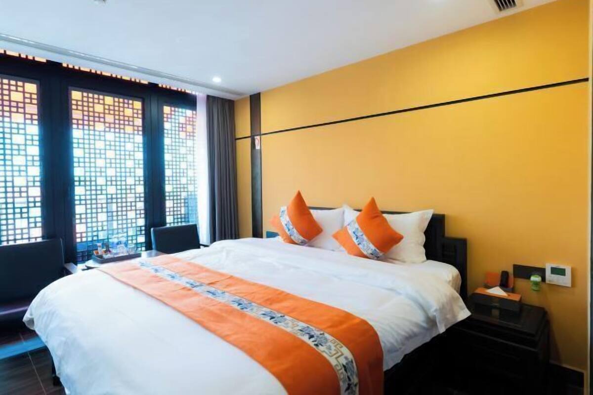 A hotel room with a large bed, a nightstand, a window with a view, and a wall-mounted thermostat.