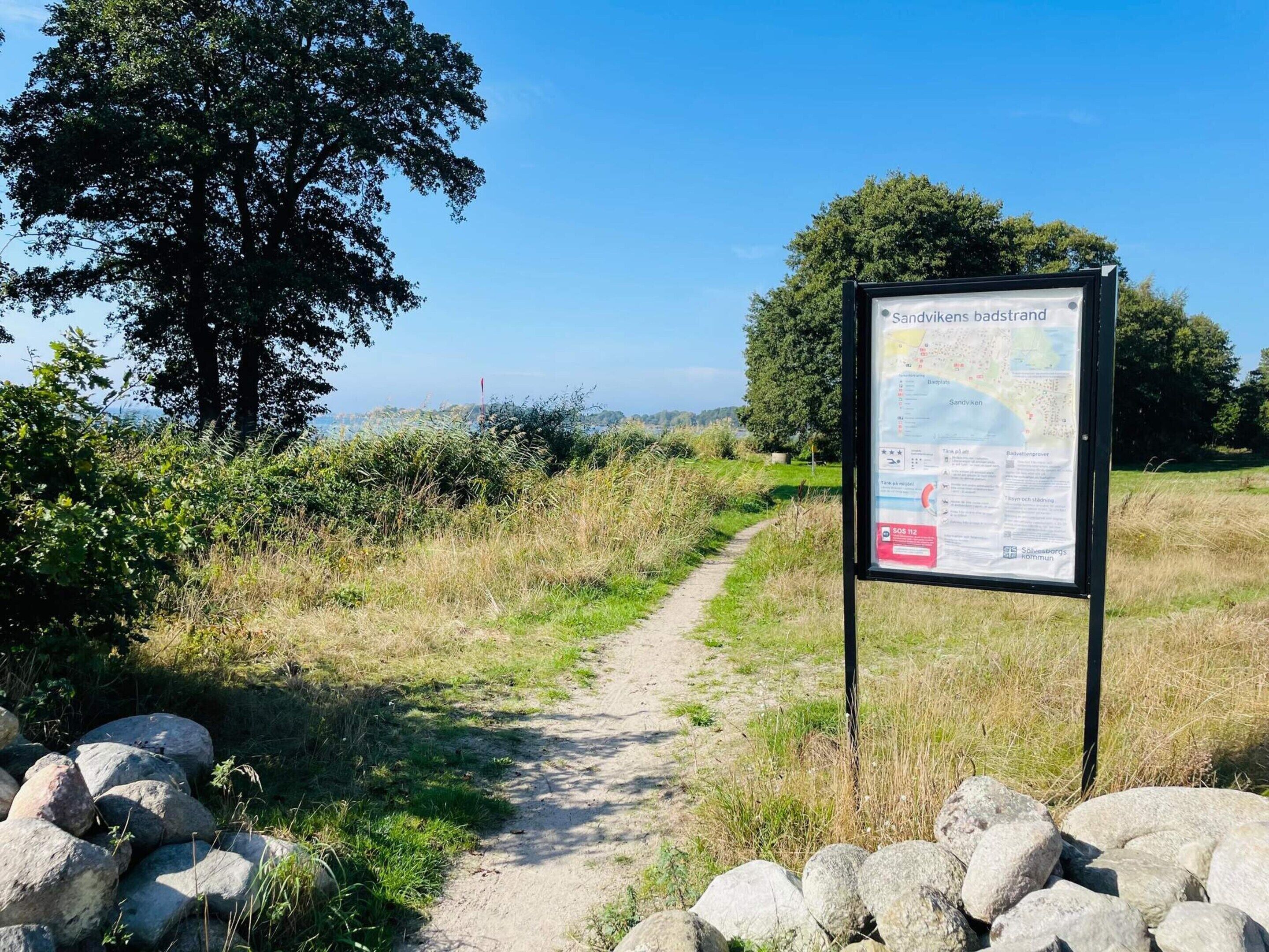 A signpost with a map and text, a dirt path, and a stone wall.