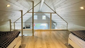 A high-ceilinged attic bedroom with wooden floors, two beds with patterned bedding, and a view of the outside. - 4 Star Holiday Home in Solvesborg (Sölvesborg)
