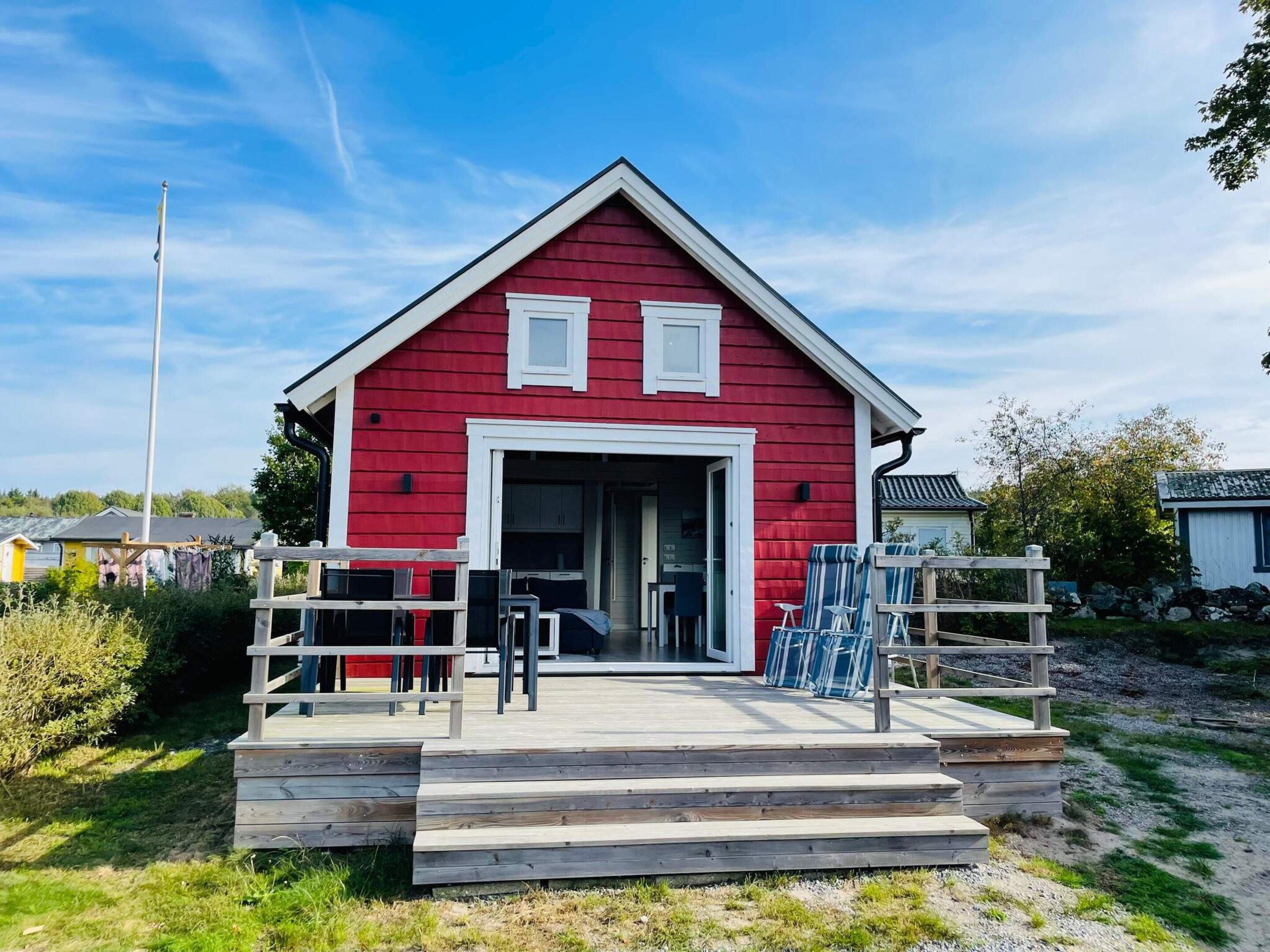 Un bâtiment rouge avec une porte et des fenêtres blanches, une terrasse en bois et un mât pour drapeau.