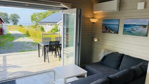 A modern interior with a sofa, a small table, and a view of a garden and house through a glass door. - 4 Star Holiday Home in Solvesborg (Sölvesborg)