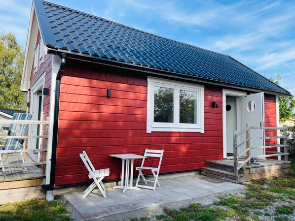 A red single-story house with a dark blue roof, white window frames, and a small porch with white chairs and a table. - 4 Star Holiday Home in Solvesborg (Sölvesborg)