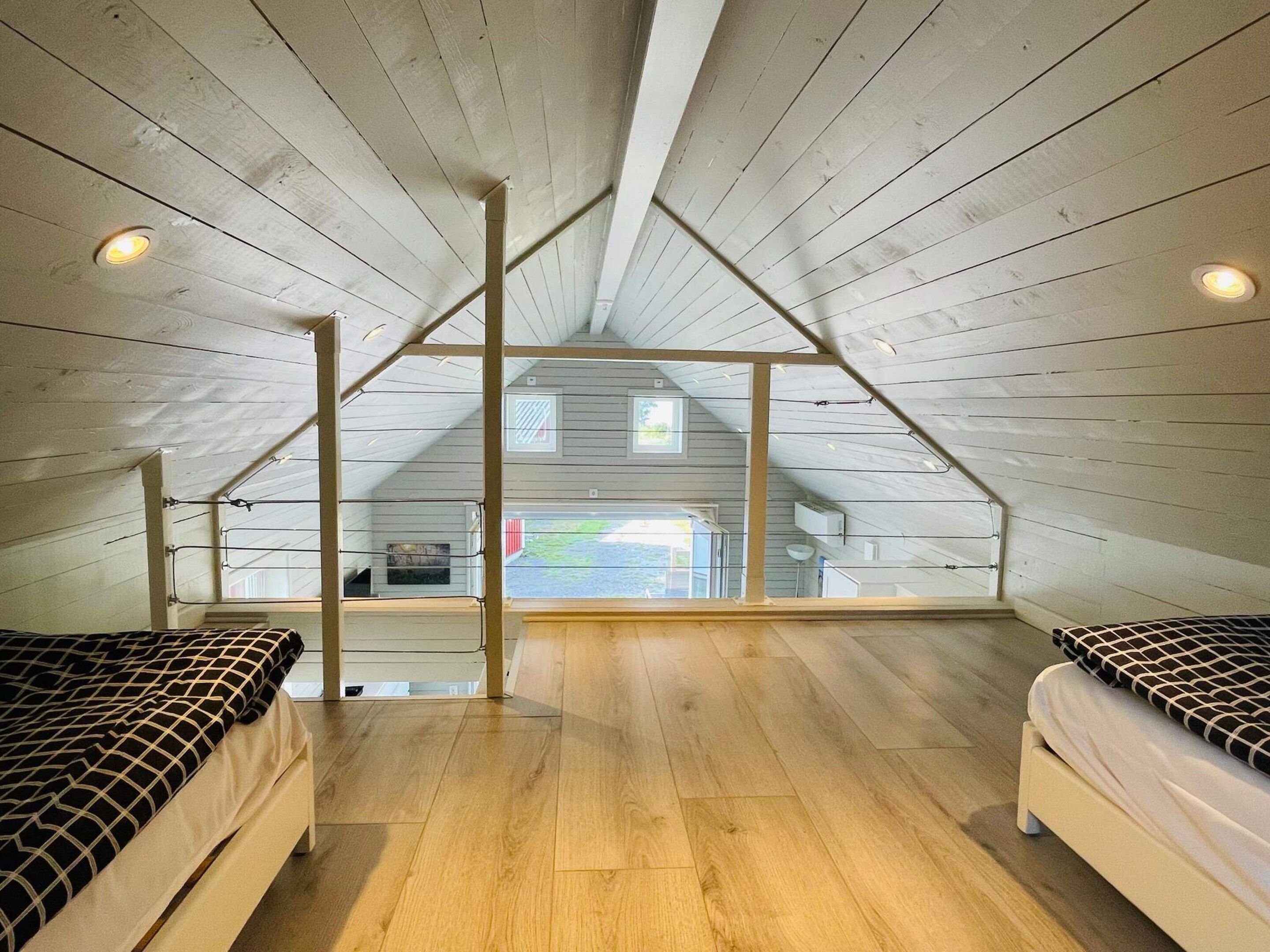 Un dormitorio en ático con techos altos, suelos de madera, dos camas y vistas al exterior.