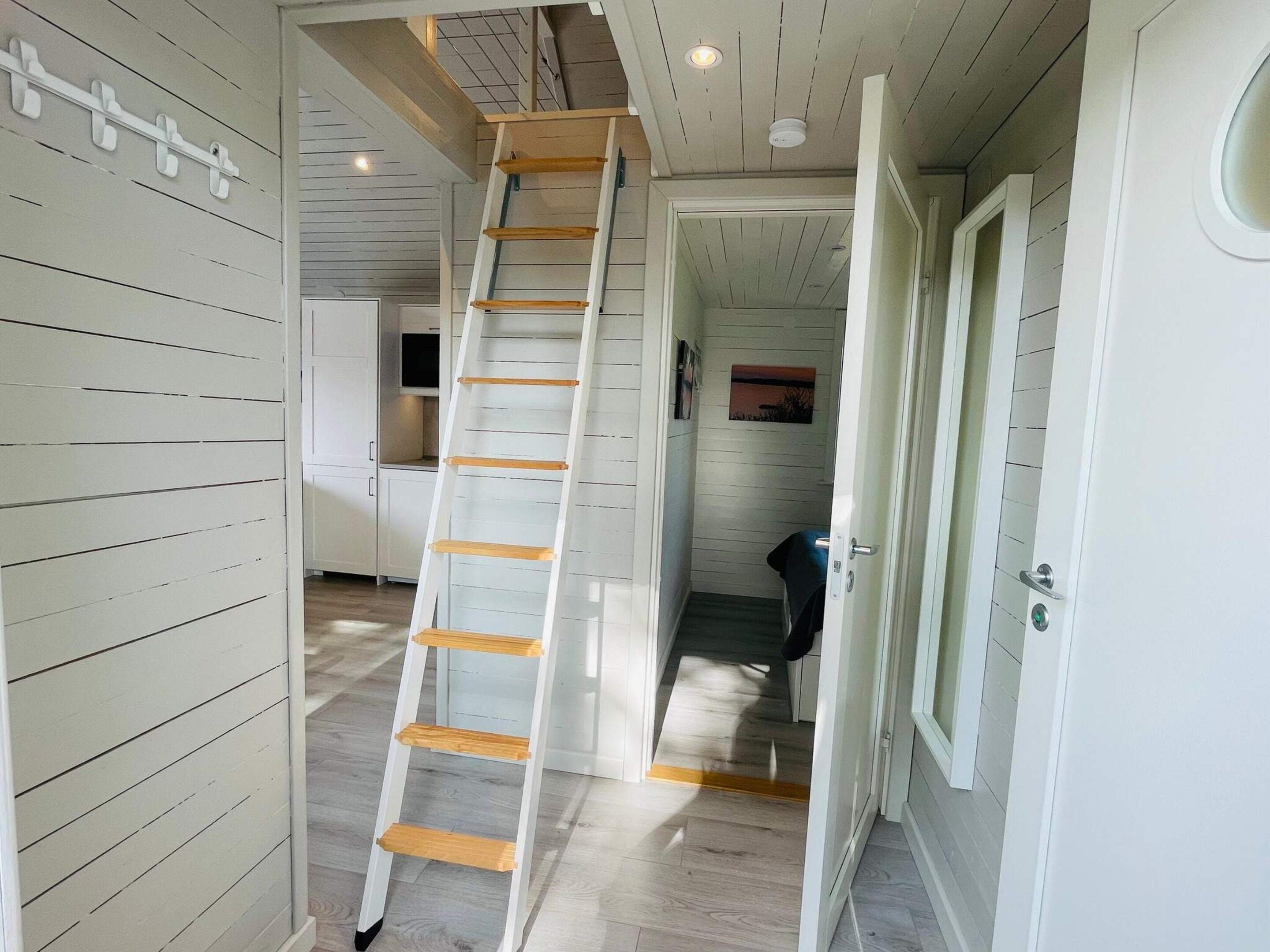 Un pasillo estrecho con una escalera de madera blanca que conduce a una zona elevada.