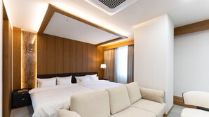 Una habitación de hotel moderna con una cama grande, un sofá y una mesita de noche.