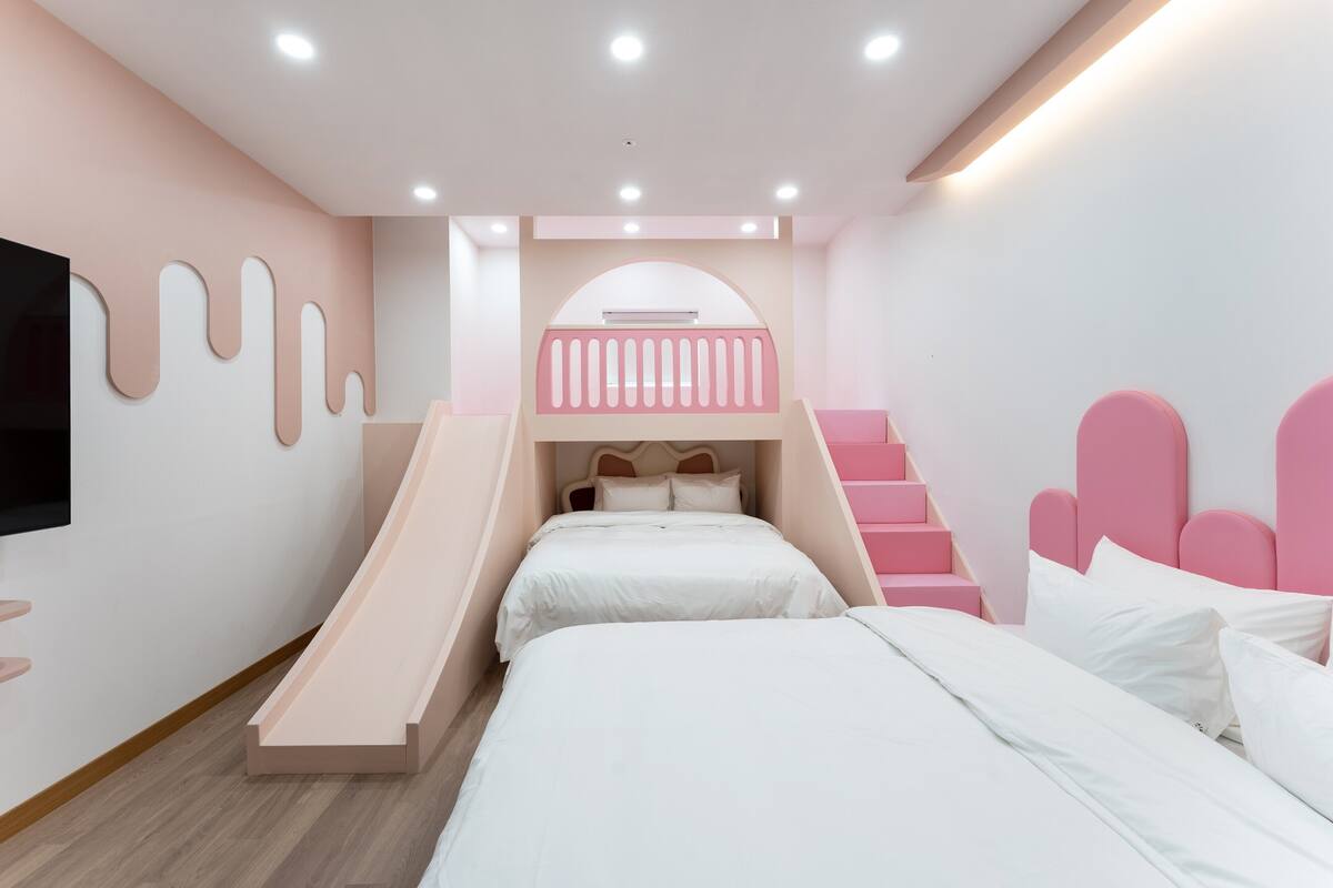 A bedroom with a bunk bed, a small desk, and a TV mounted on the wall.