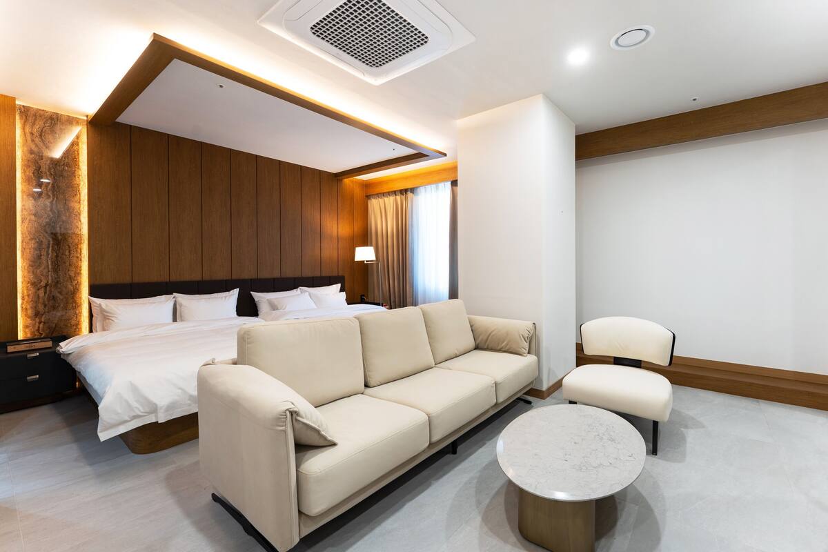 A modern hotel room with a bed, sofa, armchair, and a small round table.