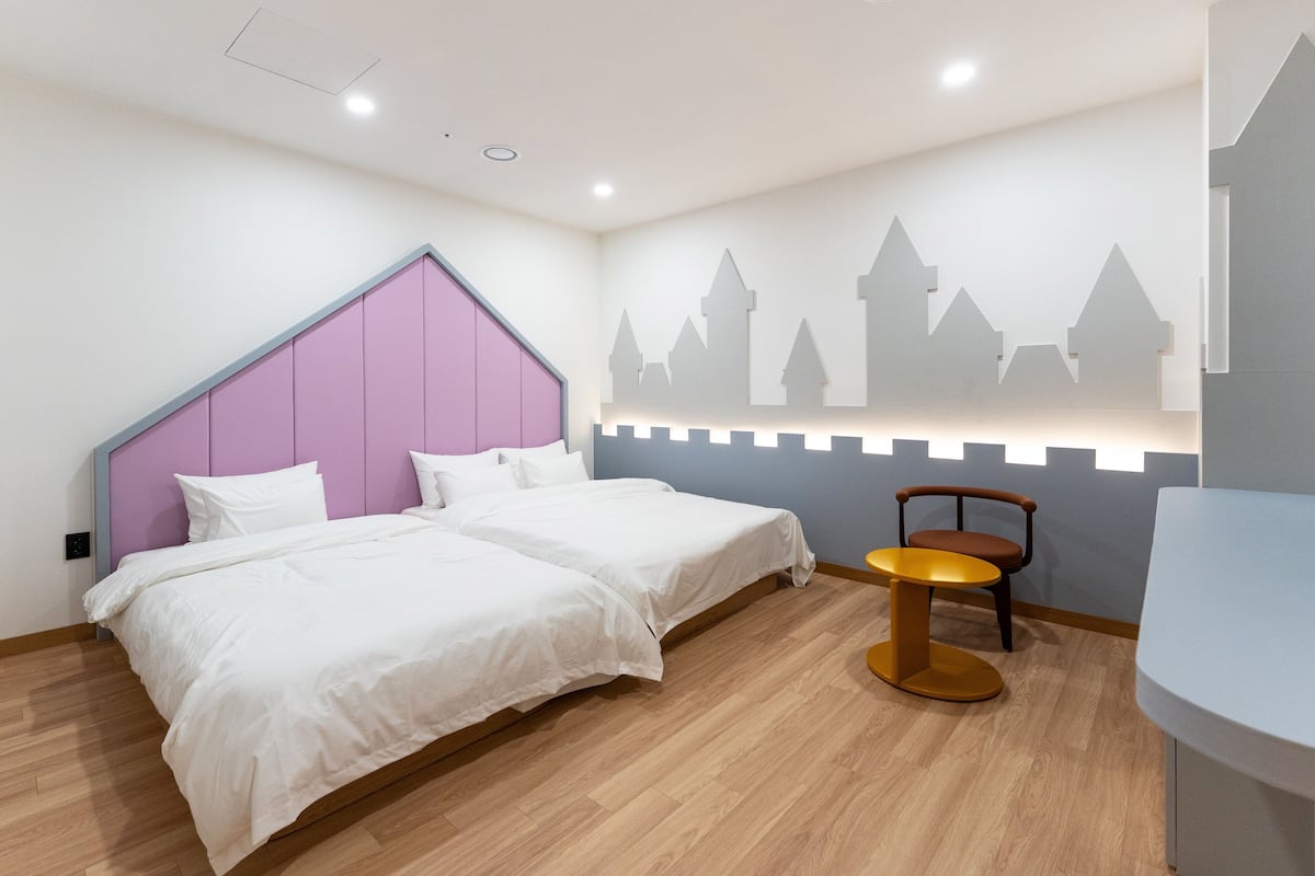 A hotel room with two beds, a wooden floor, a small round table, and a wall with a castle silhouette design.