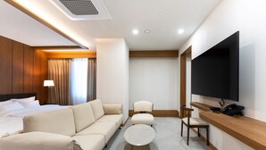 Habitación de hotel con cama, sofá, mesa de centro redonda, televisor y escritorio con teléfono.