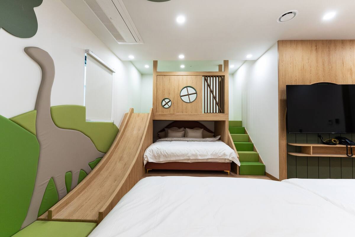 A bunk bed with a slide, green cushioned seating, a TV, and a wooden headboard.