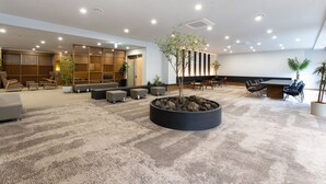 Un vestíbulo moderno con piso alfombrado, zonas de estar, una recepción y una planta grande en el centro.