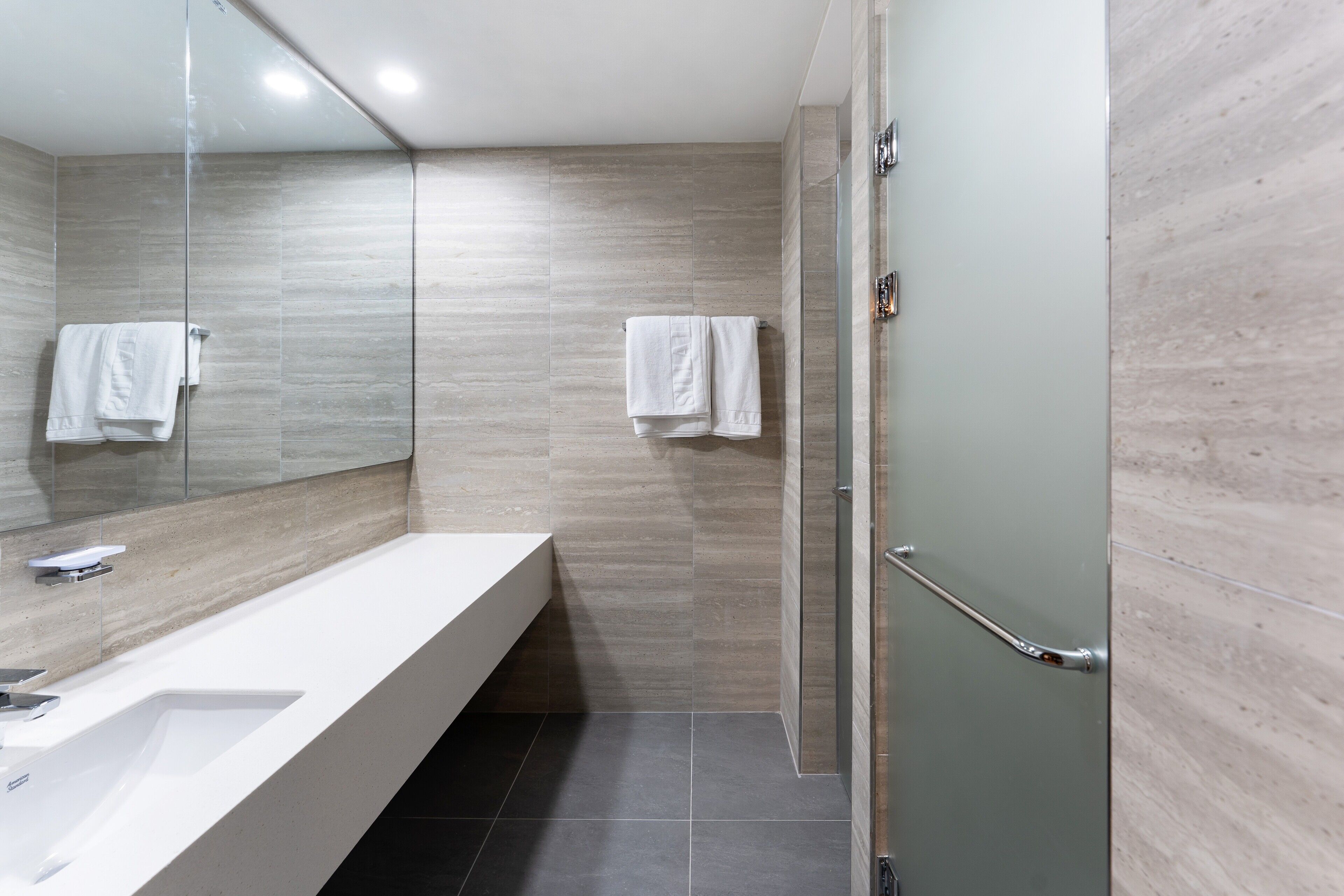 A modern bathroom with a large mirror, a white sink, and two towels hanging on the wall.