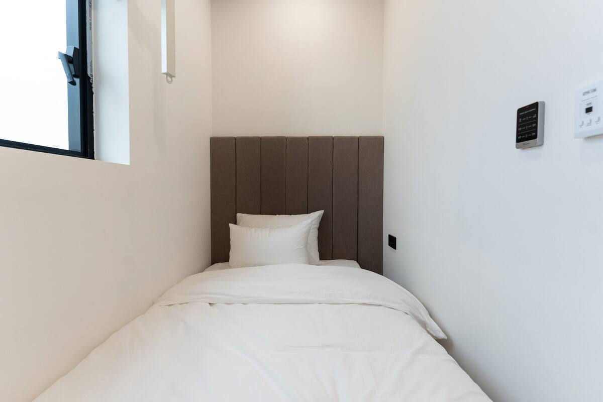 A small, neatly made bed with a wooden headboard in a minimalistic room.