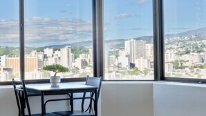 Ein Zimmer mit großem Fenster und Blick auf die Stadt, einem kleinen Tisch mit Topfpflanze und einem Stuhl.