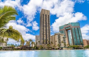 A high-rise hotel with a modern design, located near a waterfront with palm trees.