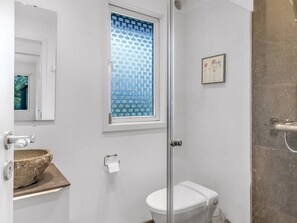 Un baño con inodoro, lavabo de piedra, ventana con persiana decorada y zona de ducha.