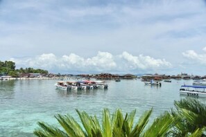 A coastal scene with boats docked at piers, clear water, and a distant shoreline with buildings. - Anaya Villa Resort (Semporna)