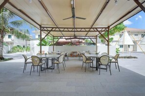 An outdoor patio with tables and chairs, a ceiling fan, and a view of buildings and greenery. - Anaya Villa Resort (Semporna)