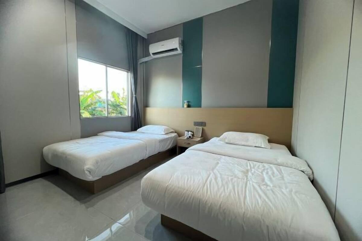 Une chambre d’hôtel avec deux lits simples, une fenêtre avec des rideaux, un appareil de climatisation et une table de chevet avec une lampe.
