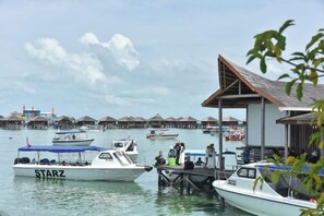 Un puerto deportivo con barcos amarrados, un muelle y bungalows sobre el agua al fondo.