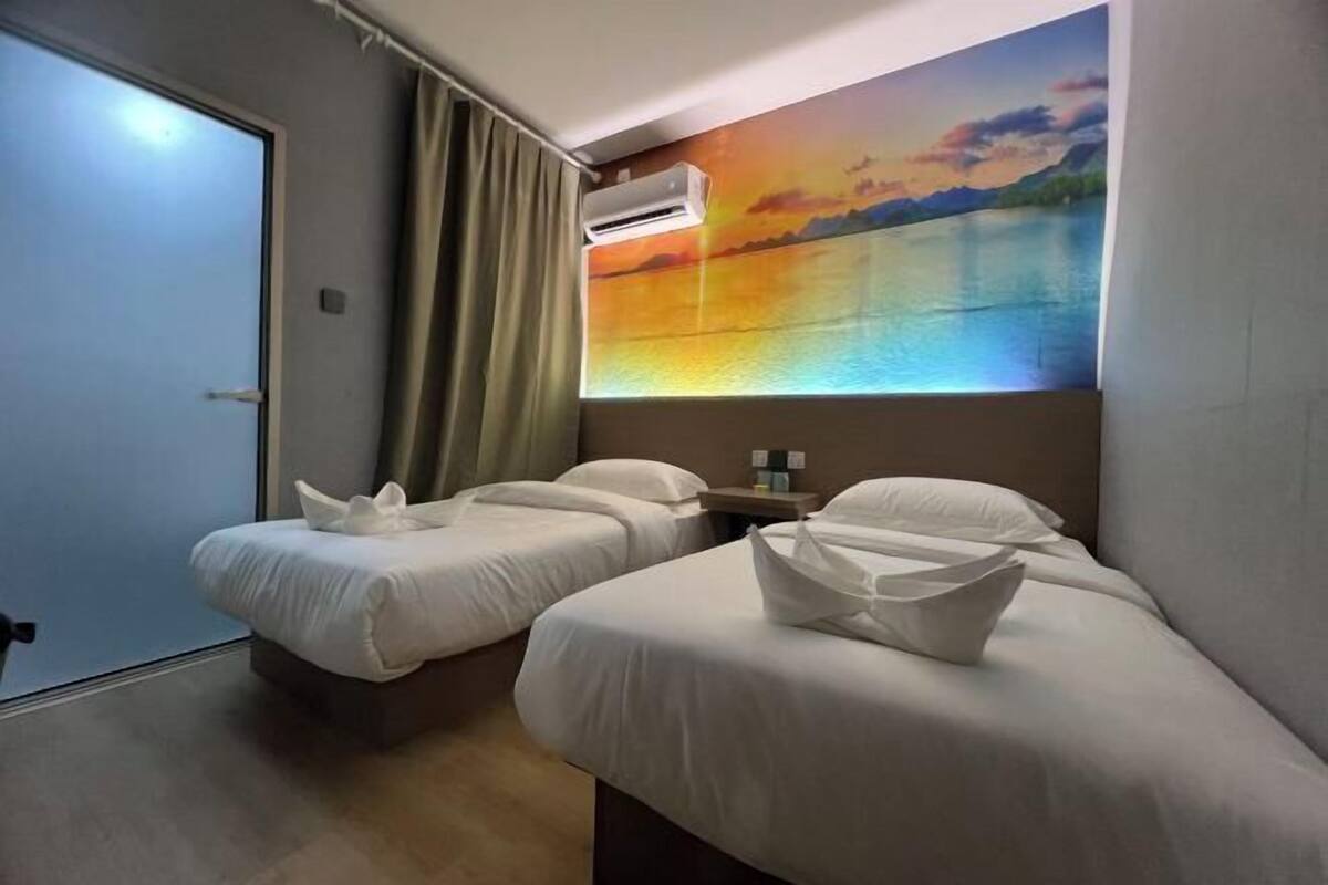 Une chambre d’hôtel avec deux lits, un tableau représentant un coucher de soleil sur l’eau accroché au mur, un climatiseur et une porte.