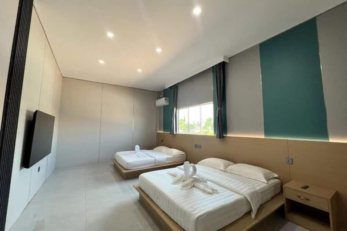 A modern hotel room with two beds, a flat-screen TV, and a window with curtains.