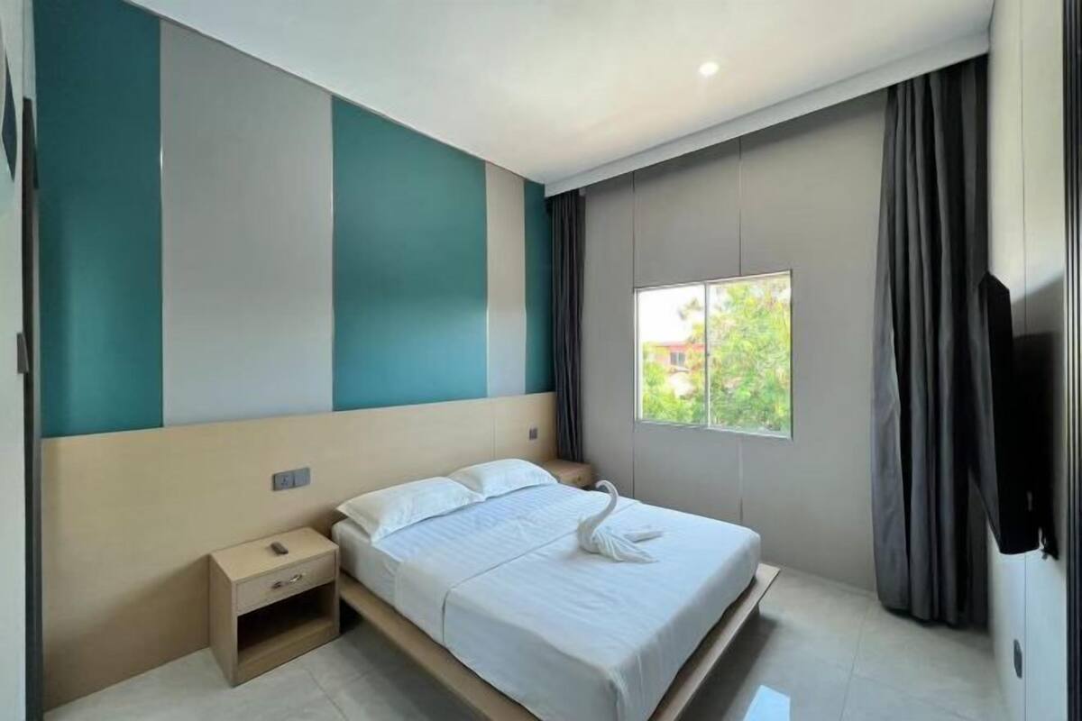 Une chambre d’hôtel moderne équipée d’un lit, d’une table de chevet, d’une fenêtre avec des rideaux et d’un téléviseur à écran plat.