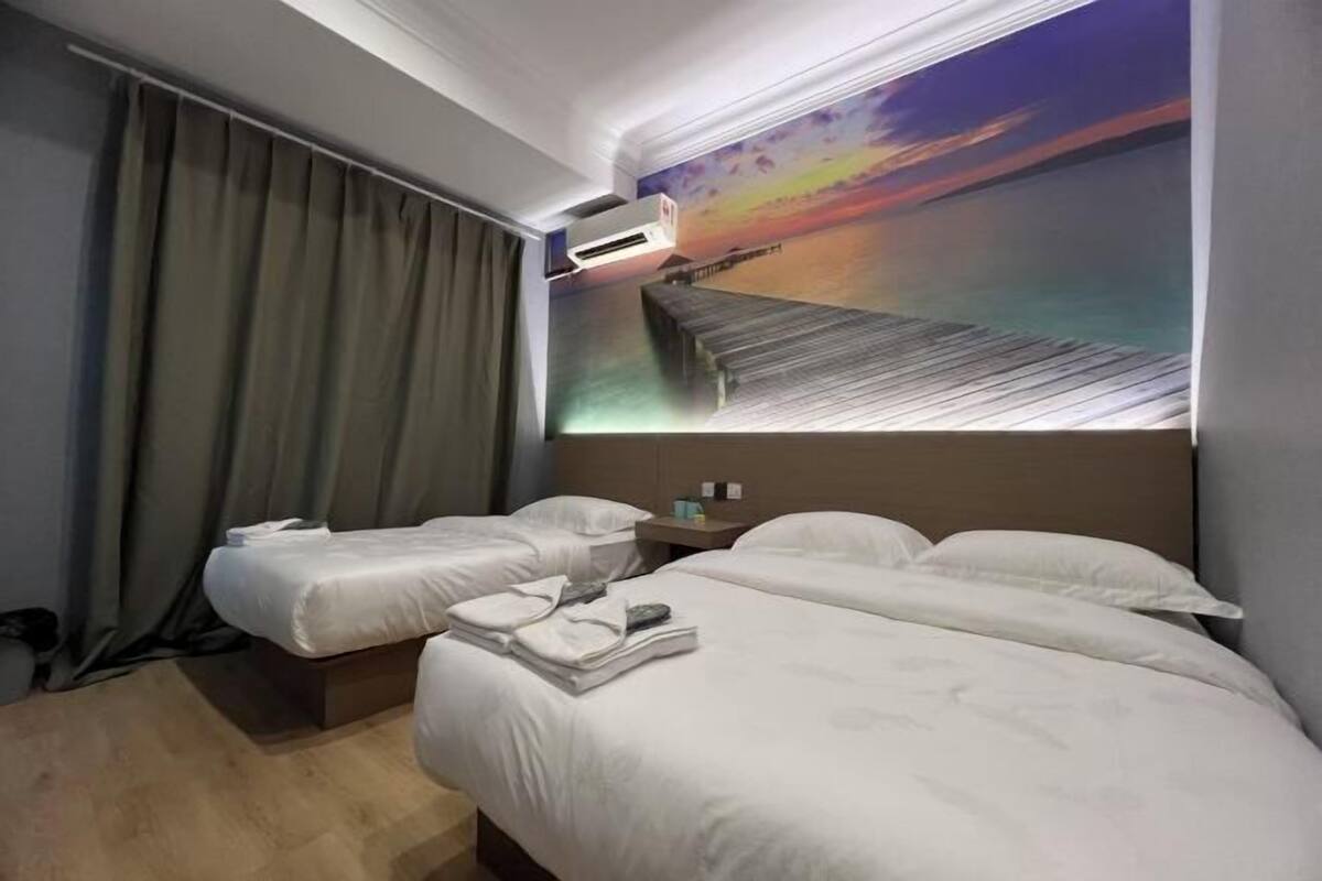 Une chambre d’hôtel avec deux lits, une grande fresque représentant un coucher de soleil sur l’eau et un appareil de climatisation.