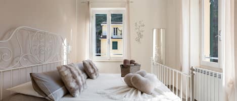 A bedroom with a bed, a window, a radiator, and a view of buildings outside.