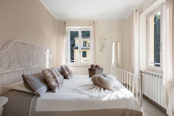 A bedroom with a bed, a window, a radiator, and a view of buildings outside.