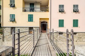 A narrow pathway leading to a building with multiple balconies and green shutters.
