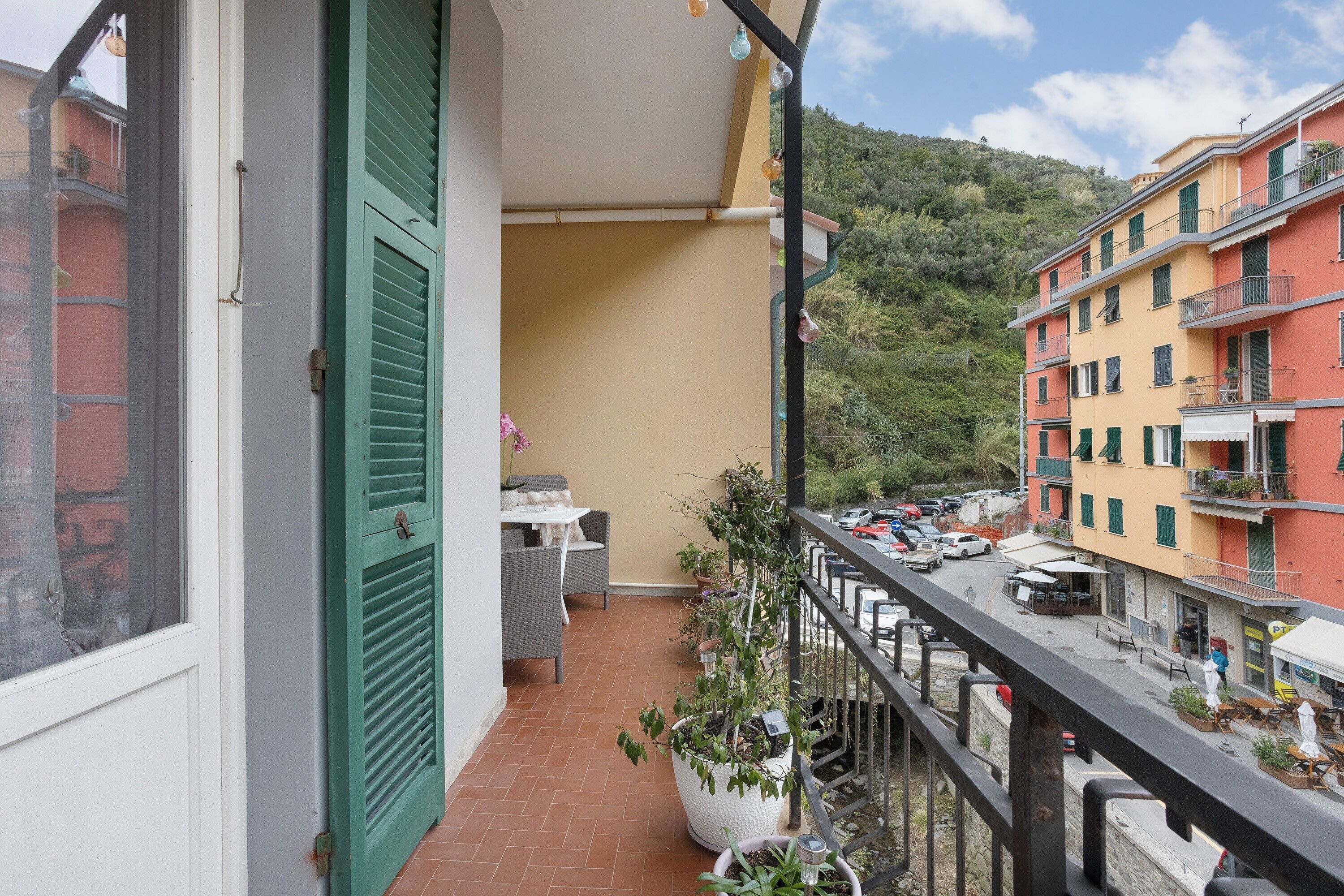 A balcony with a view of a street, a table with chairs, and potted plants.