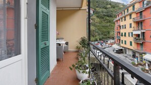 Un balcon donnant sur une rue, une table avec des chaises et des plantes en pot.