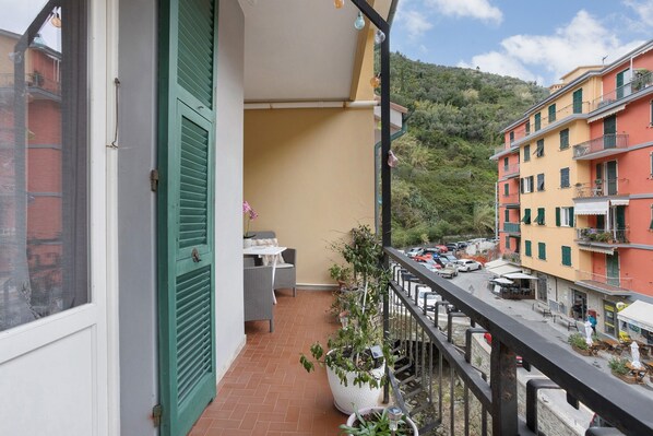 A balcony with a view of a street, a table with chairs, and potted plants.