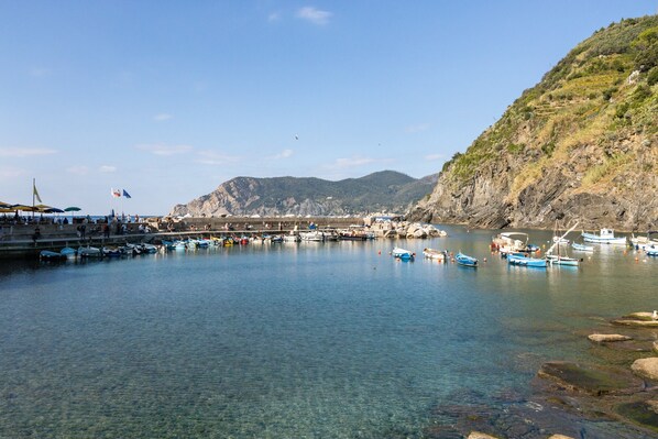 A coastal marina with boats docked, a pier, and a mountainous backdrop.
