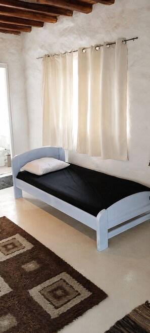 Una cama individual con cabecera y piecera blancos, colchón negro y una alfombra de diseño marrón y blanco.