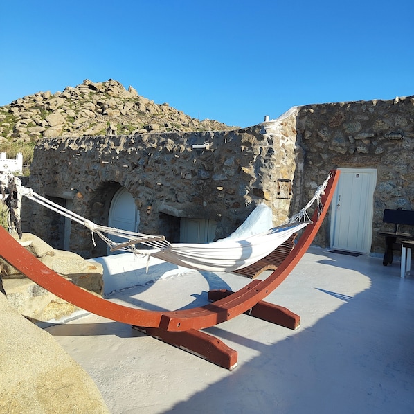 A hammock in a stone-walled courtyard with a door and a white wall in the background.