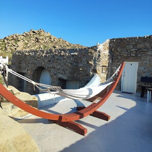 A hammock in a stone-walled courtyard with a door and a white wall in the background.