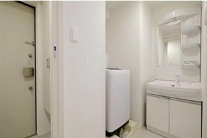Un baño con una puerta blanca, dispensador de toallas, lavamanos con espejo y un armario blanco.