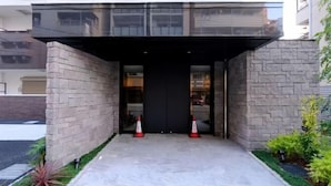 Una entrada moderna de edificio con fachada de vidrio, paredes de piedra y sendero de hormigón.