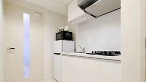 Cocina compacta con armarios blancos, microondas, fregadero y estufa a gas.