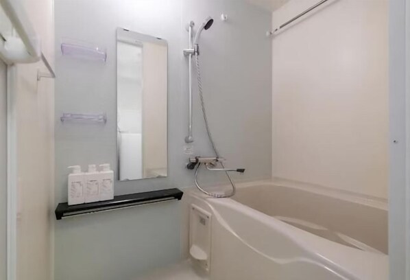 A bathroom with a bathtub, a shower, a mirror, and a shelf with toiletries. - RAKUYADO DAIKOKUCHO (Osaka)