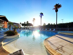 A swimming pool with lounge chairs and palm trees, surrounded by a fence. - Cap Hermès residence for 4 people, superb sea view, 2-bedroom, air-conditioned, swimming pool, direct beach access, private parking, large balcony (Fréjus)