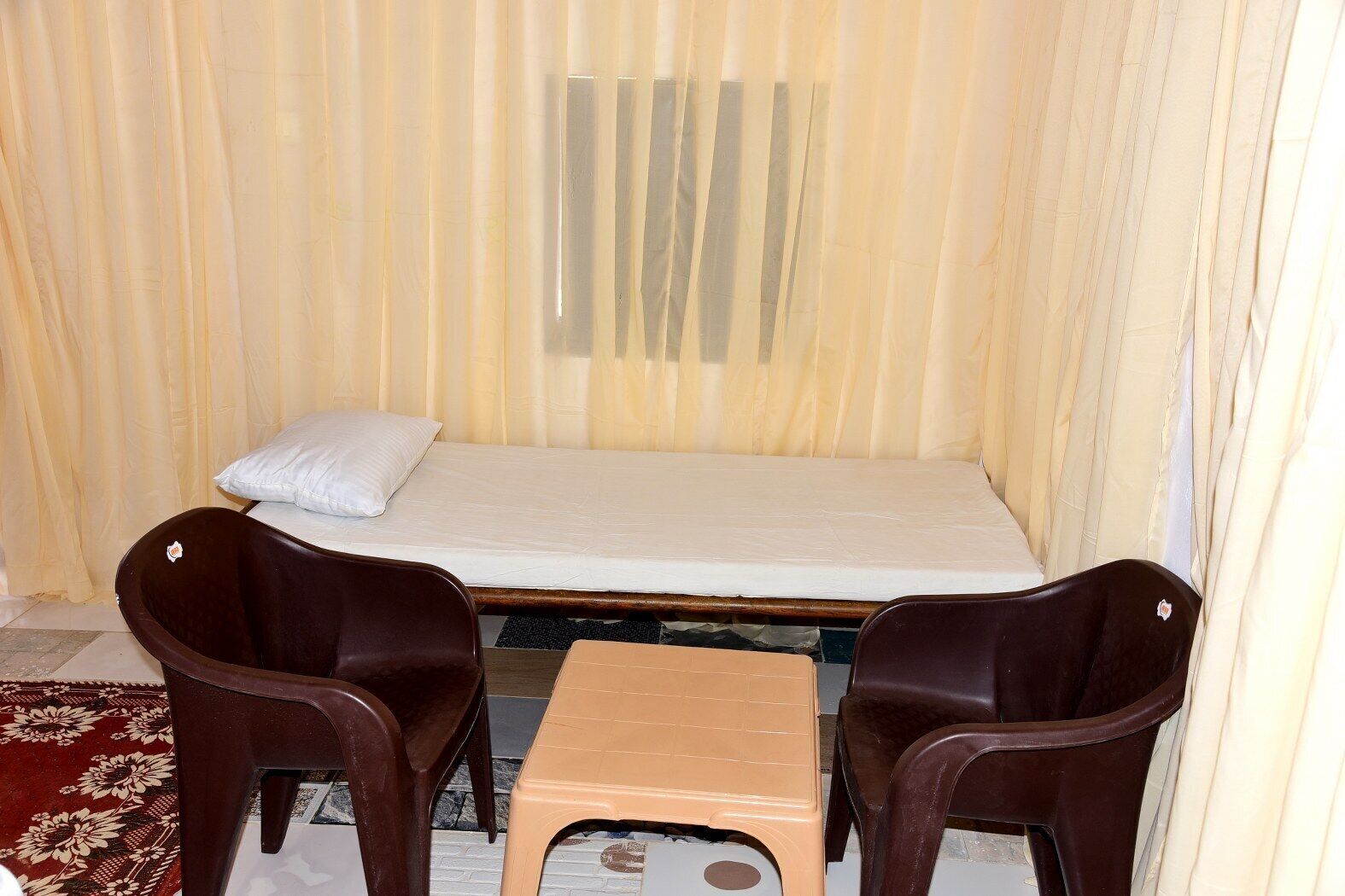 A small, single-bed room with a mattress, two chairs, and a small table.